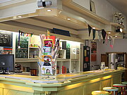 Der Thekenbereich des Jugendzentrums mit bunten Barhockern und Postkartenständer.