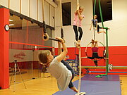 In einer bunten Halle üben vier Kinder Luftakrobatik.
