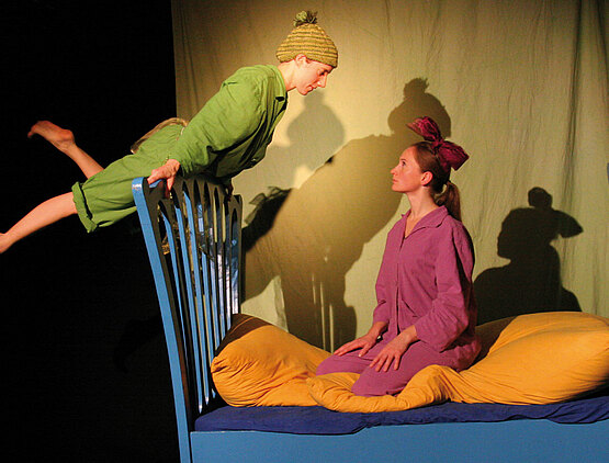 Bühnenszene mit zwei Schauspielerinnen: Peter Pan fliegt auf Wendys Bettgestell.