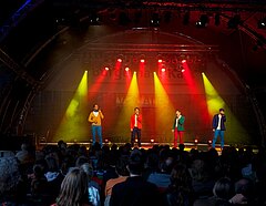 Bühne mit Lichtshow und vier männlichen Sängern in farbig auffallenden Anzügen