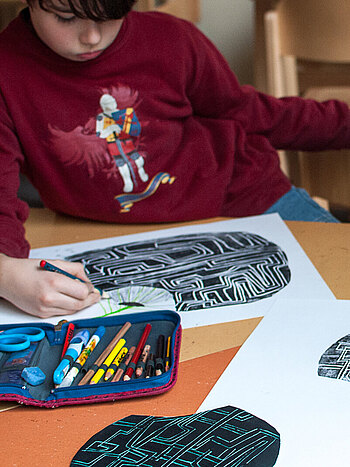 Ein Junge kopiert konzentriert ein Labyrinth im Rahmen eines Tagebuchprojekts.