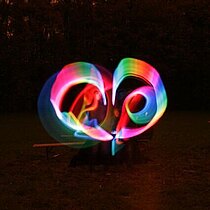 Lichtkunst: Regenbogenfarbige Lichtwirbel vor nachtschwarzem Hintergrund.