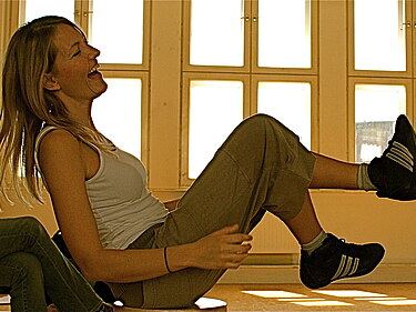 Eine junge Schauspielerin lacht beim Training in einer hellen Halle.
