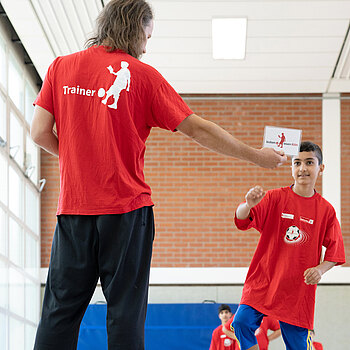 Ein Trainer und ein Junge stehen sich in roten Motto-T-Shirts gegenüber.