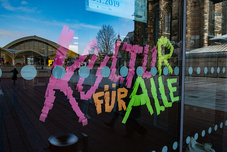 Die Fotokünstlerin Sandy Craus hat an die Scheibe des Museum Ludwig aus Hunderten von Haftnotizzetteln in Pink, Orange, Neongelb Neongrün die Botschaft geklebt "Kultur für Alle". In der Scheibe spiegelt sich die Ostseite des Doms.