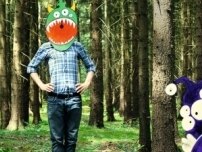Ein Mensch steht mit grüner Fantasiemaske und weit aufgerissenem Maul im Wald.