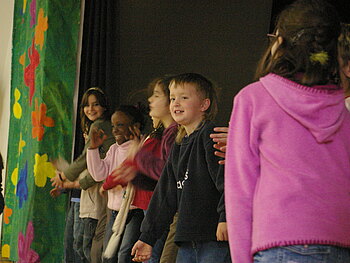 Fünf Kinder stehen rechts neben einem bunten Theatervorhang.