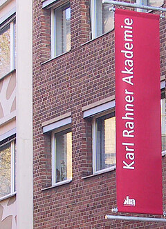 Außenfassade mit dem roten Banner der Karl Rahner Akademie.