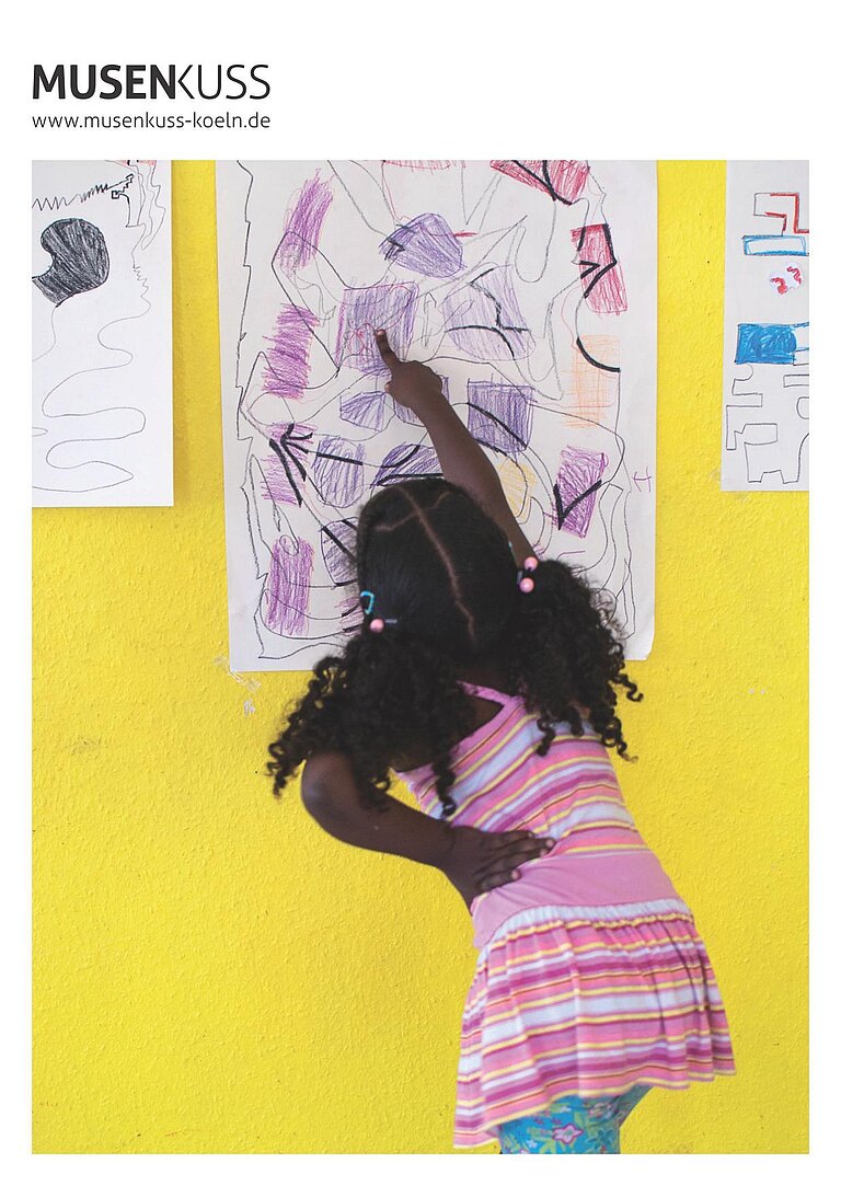 Ein Mädchen in Rückenansicht steht vor einer gelben Wand und zeigt auf ein Bild.  