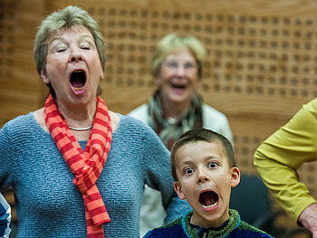 Chor in Aktion: ein Junge und zwei ältere Damen singen engagiert