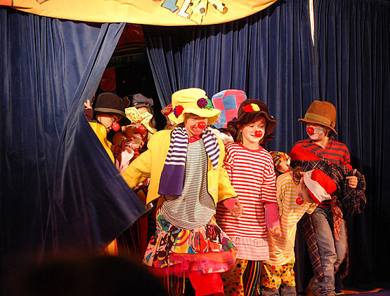 Kleine Clowns drängen durch einen Zirkusvorhang in die Manege.