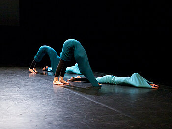 Bühnenszene Tanzperformance: drei Tänzerinnen bilden eine Figur in grünen Kostümen