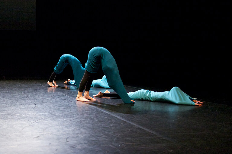 Bühnenszene Tanzperformance: drei Tänzerinnen bilden eine Figur in grünen Kostümen 