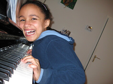 Ein lachendes Mädchen beugt sich über eine Klaviertastatur.