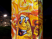 Grafitti-Kunst in gelb-orange leuchtet angestrahlt in der nächtlichen Stadt.