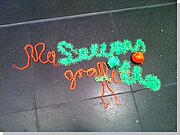 Kinder-Grafitti aus dicken grünen und orangefarbenen Wollfäden  auf dem Museumsboden.