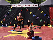 Ein Mädchen im Kostüm des Zirkusdirektor jongliert in einer wimpelgeschmückten Arena im Freien.