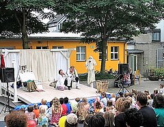 Open Air Theatersituation auf weiß gestrichener Bretterbühne: Mann und Frau in dramatischer Pose