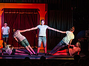 Akrobatik mit drei Männern auf rot beschienener Bühne