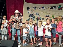 Bühnensituation: Kinder im Vorschulalter und ein  Mann mit Strohhut, Hawaiihemd und Gitarre.